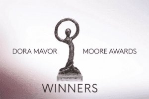 An image of a Dora Mavor Moore Award on a white background. The statue displays a bronze humanoid figure, its arms raised above its head to create a circle. Surrounding the statue is text reading "Dora Mavor Moore Awards" and below reads "winners"